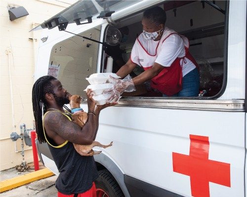 red cross volunteer handing meals and snacks to a man from an emergency response vehicle